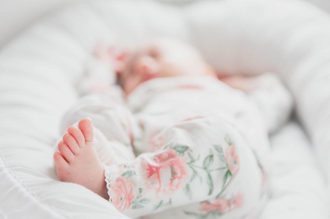 Baby in white and red floral onesie lying on bed from Tuva Mathilde Løland on Unsplash