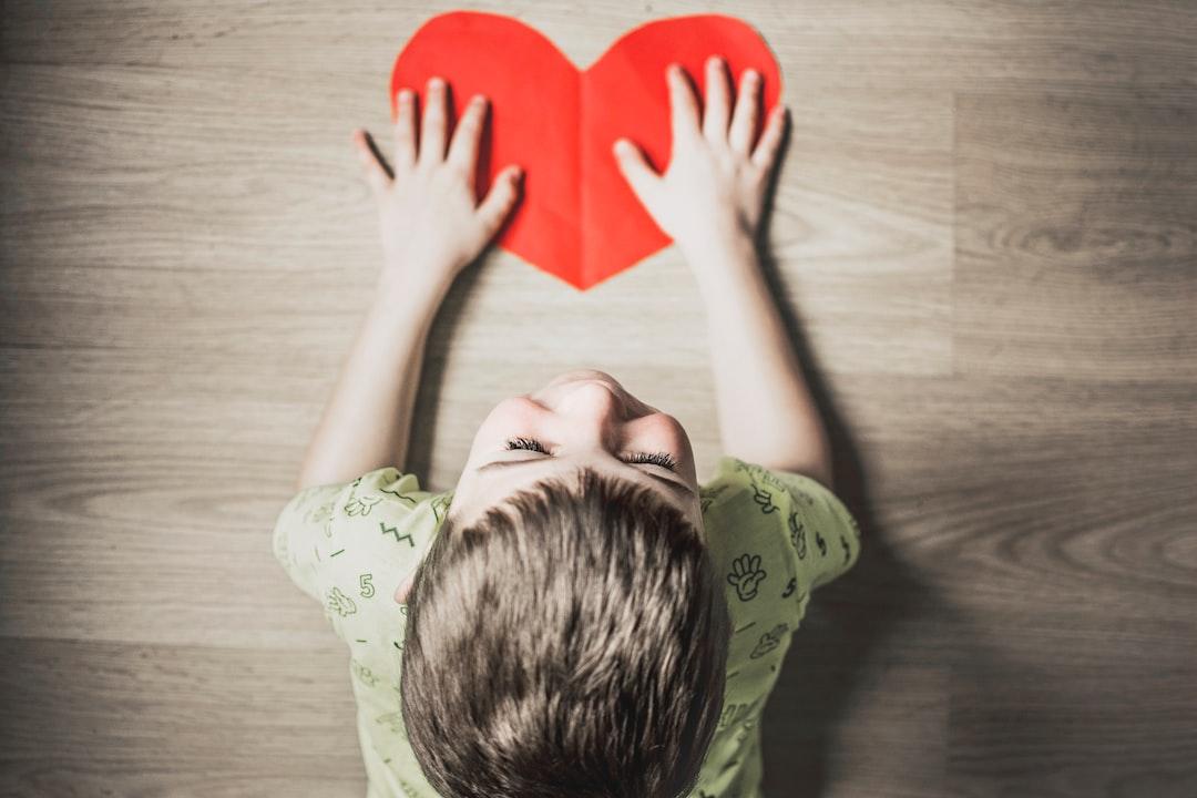 Boy in green shirt holding red paper heart cutout on brown table from Anna Kolosyuk on Unsplash Ngạc nhiên nho nhỏ mỗi ngày