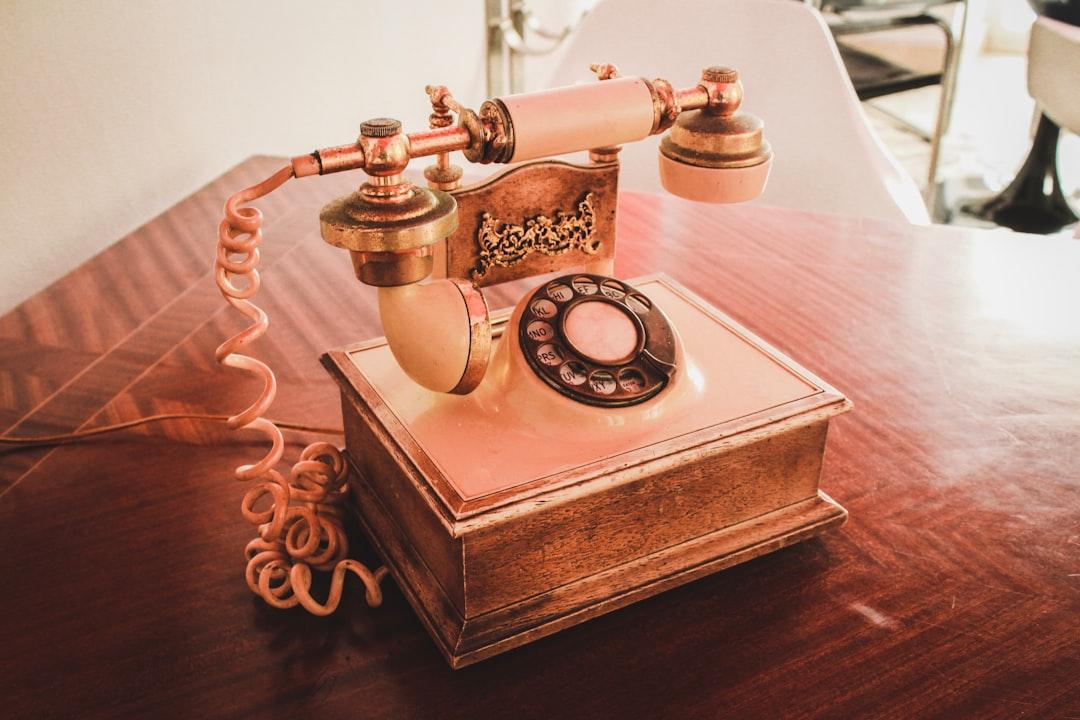 White and brown rotary telephone on brown wooden table from Louis Hansel on Unsplash
