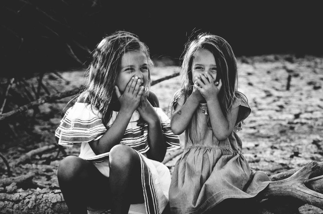 Grayscale photography of two girls closing their mouths from Caroline Hernandez on Unsplash