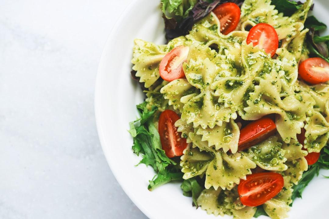 Pesto pasta with sliced tomatoes served on white ceramic plate from Eaters Collective on Unsplash