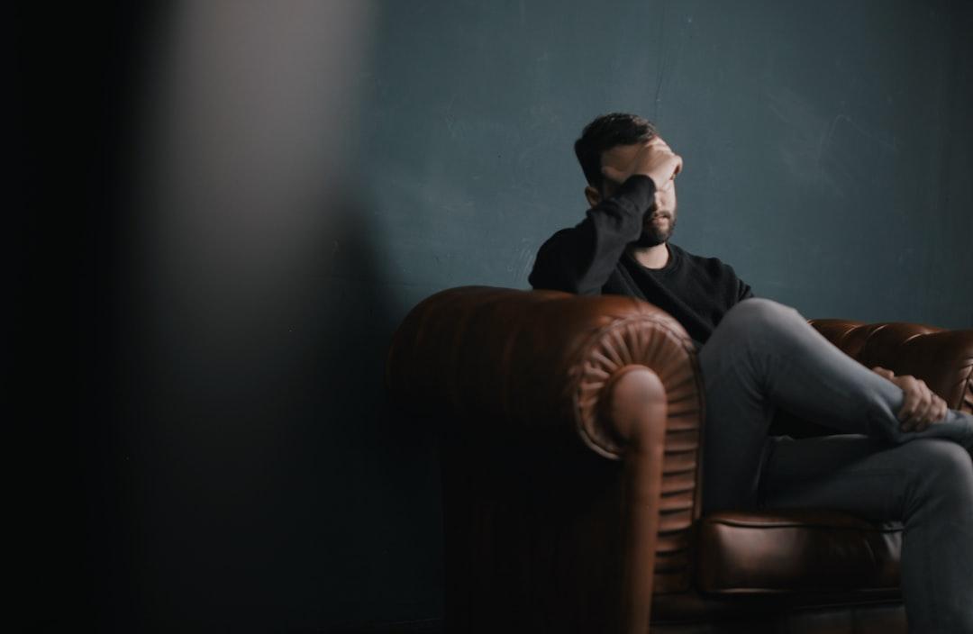 A man holds his head while sitting on a sofa from Nik Shuliahin 💛💙 on Unsplash