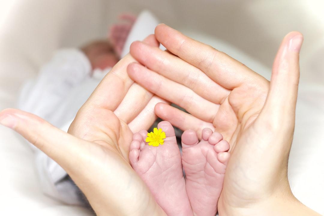 Person holding baby's toe with yellow petaled flower in between from Manuel Schinner on Unsplash