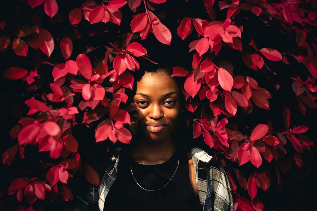 A woman standing in front of a tree with red leaves from Trésor Kande on Unsplash