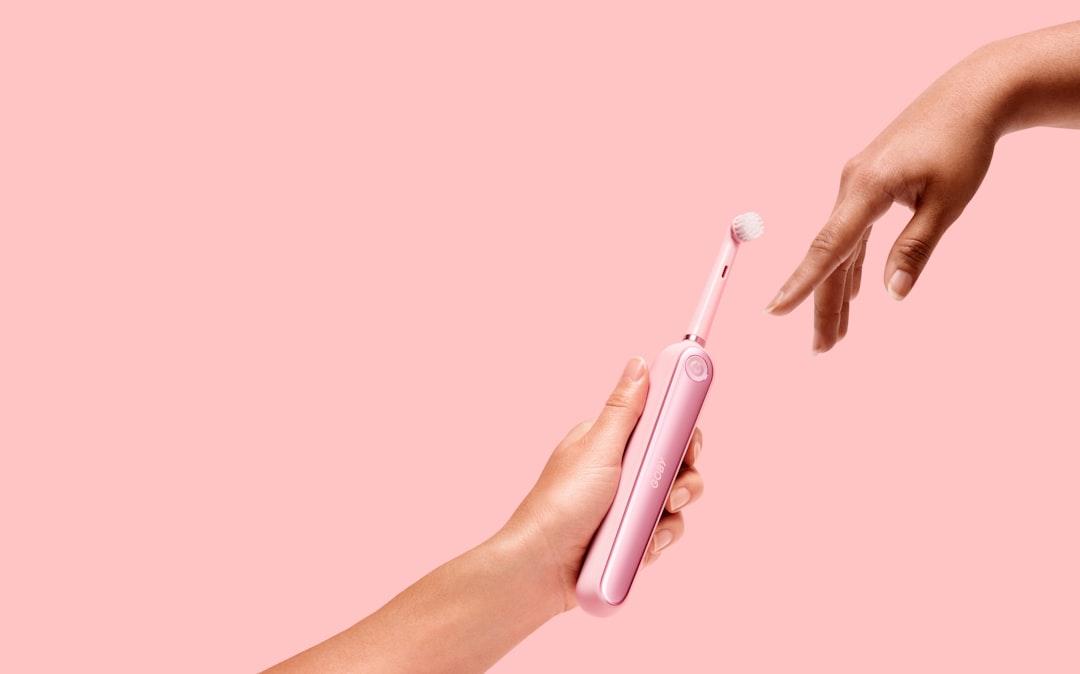 Person holding pink electric toothbrush from Goby on Unsplash
