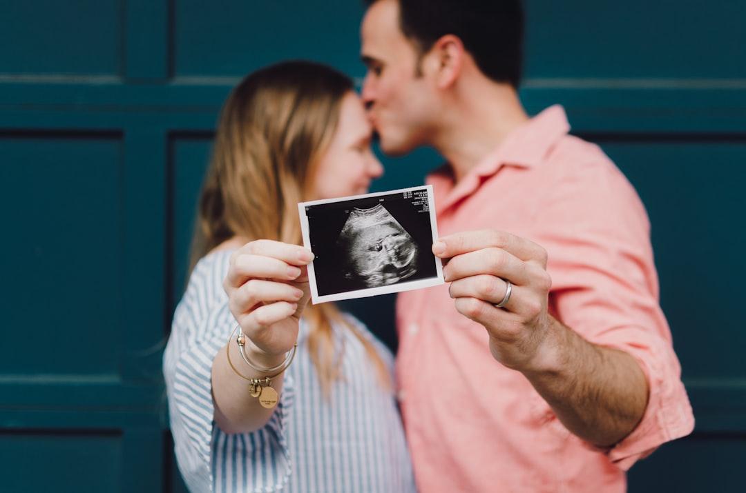 Man kissing woman's forehead white holding ultrasound photo from Kelly Sikkema on Unsplash