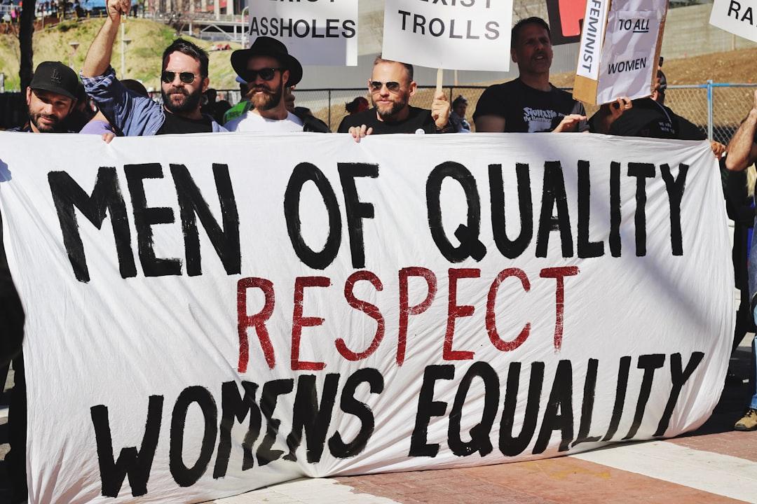 Men holding white, black, and red men of quality respect womens equality banner on road from Samantha Sophia on Unsplash