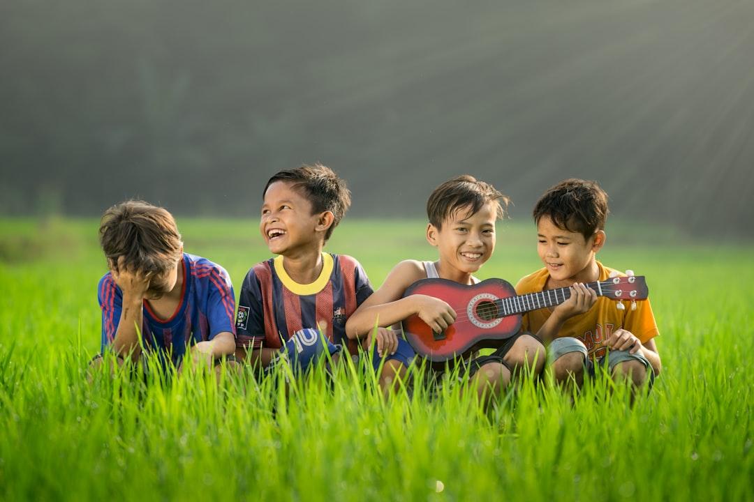 four boys laughing and sitting on grass during daytime Mút tay